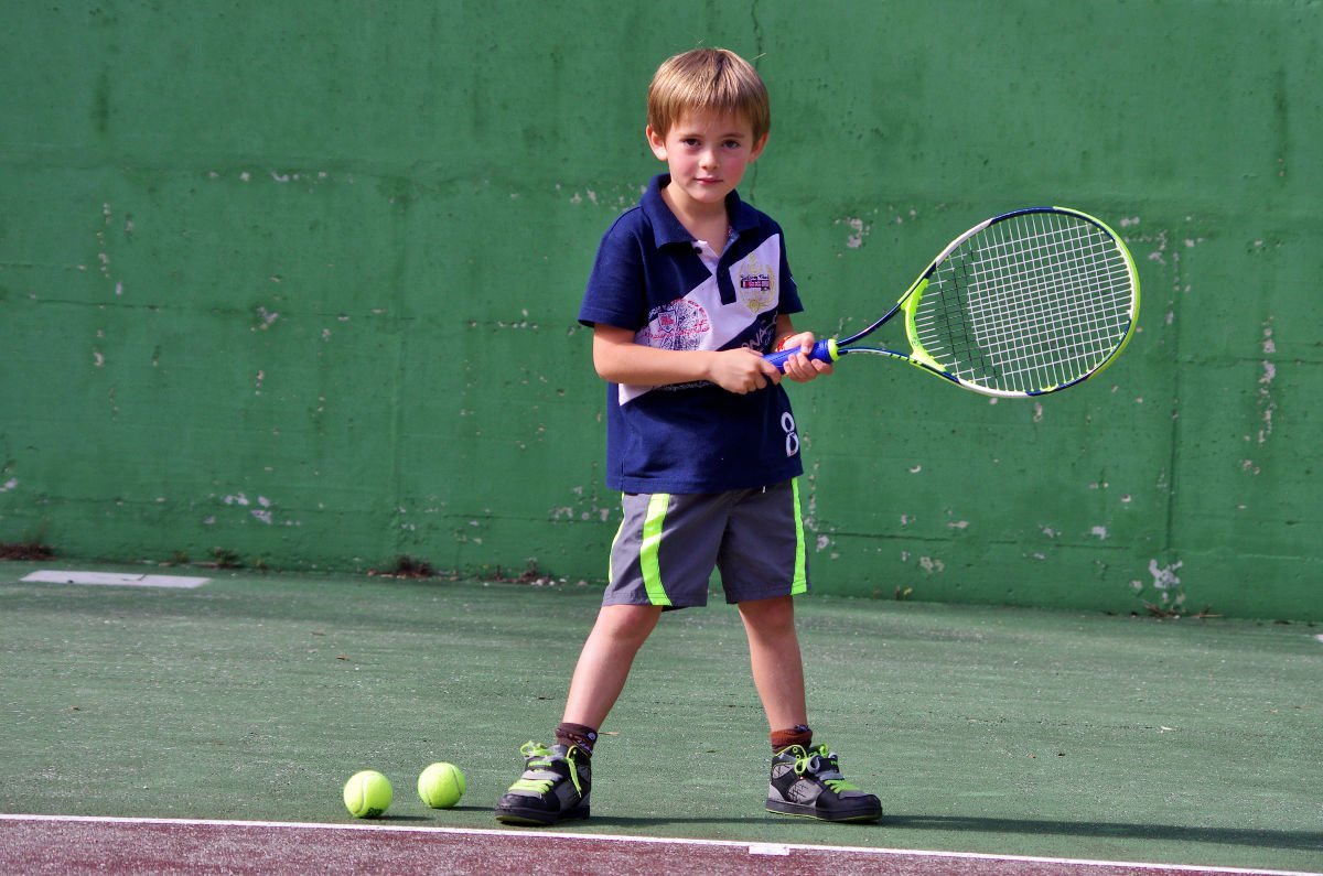 Foto eines Jungen mit Tennisbällen und einem Kindertennisschläger