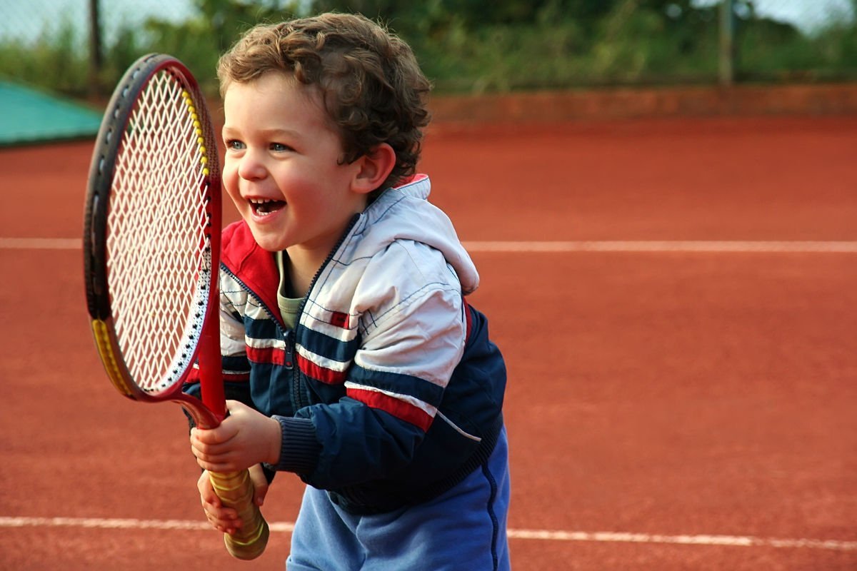 Foto eines Kindes mit einer Trainingsjacke und einem Tennisschläger