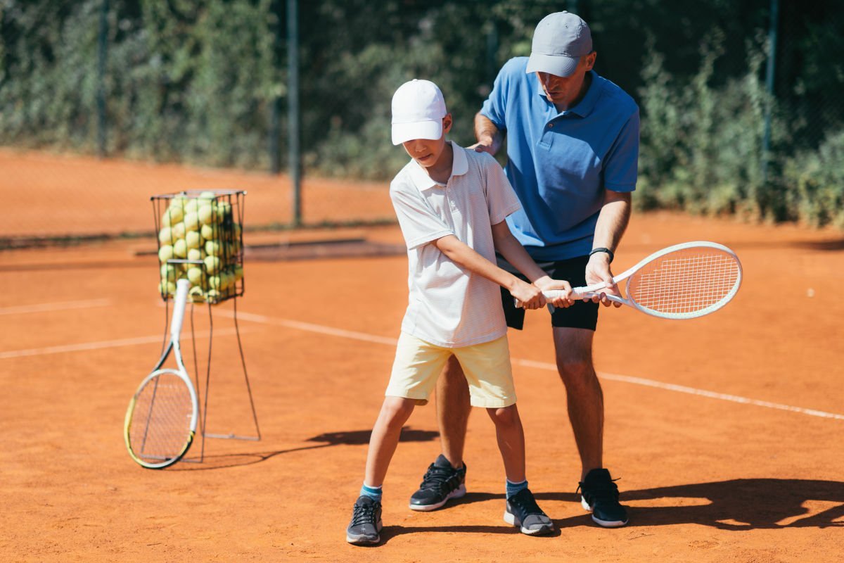 Foto de un entrenador de tenis con un estudiante en la cancha de tenis